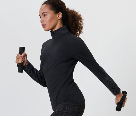 Žena v čiernom športovom oblečení drží v každej ruke 2 bežecké a gymnastické činky.