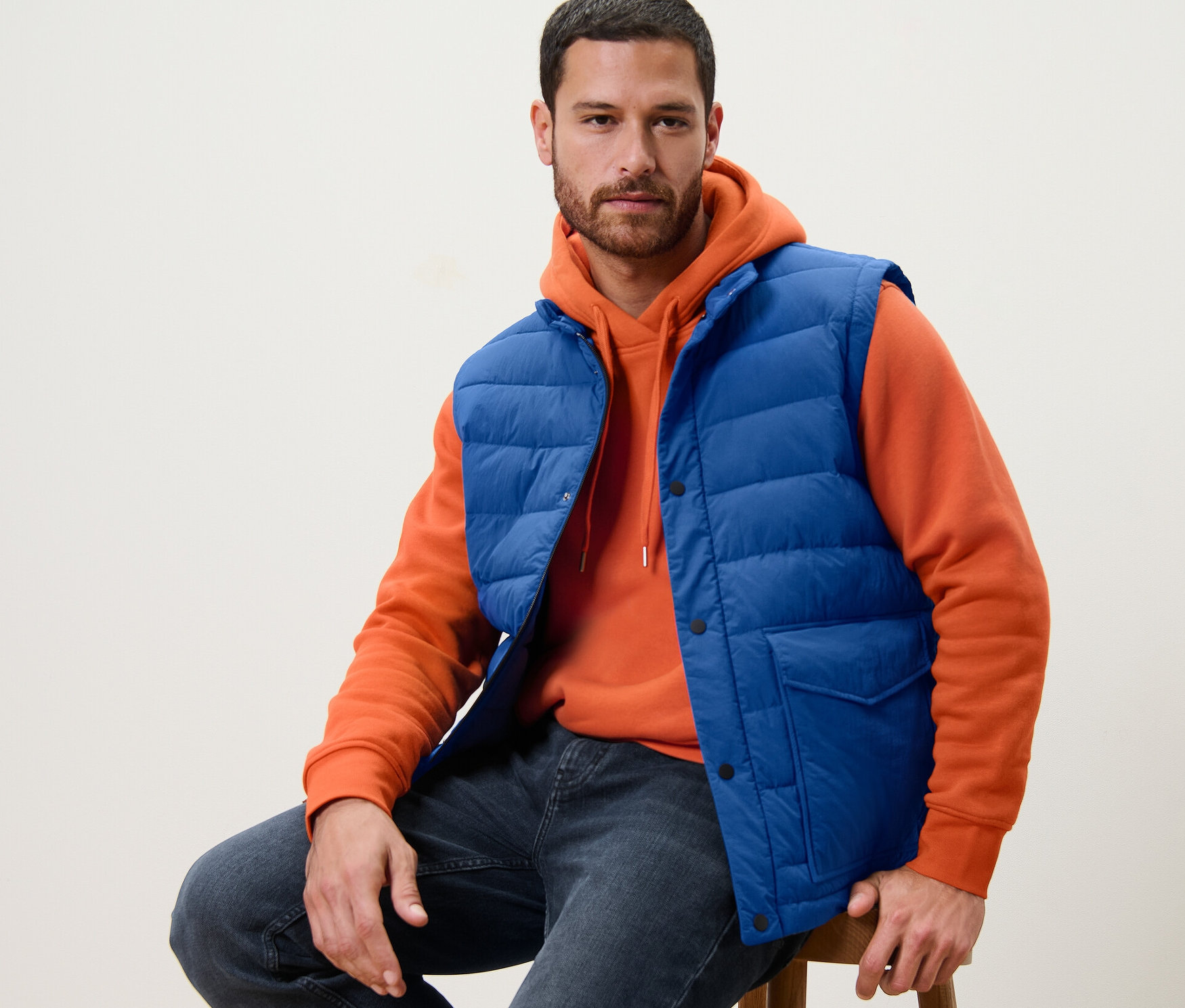 Muž sedí na stoličke v modrej prešívanej veste.