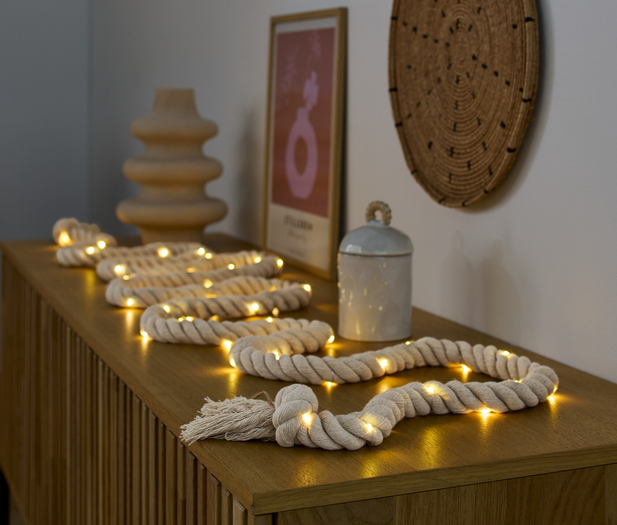 LED svetelná reťaz leží na drevenej komode vedľa vázy a dózy.