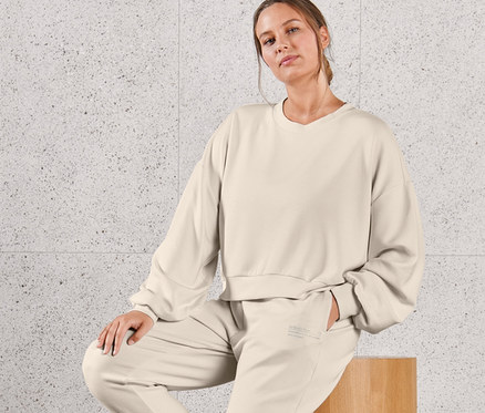 Žena sedí na drevenej stoličke a má na sebe obzvlášť mäkkú mikinu a obzvlášť mäkké teplákové nohavice.