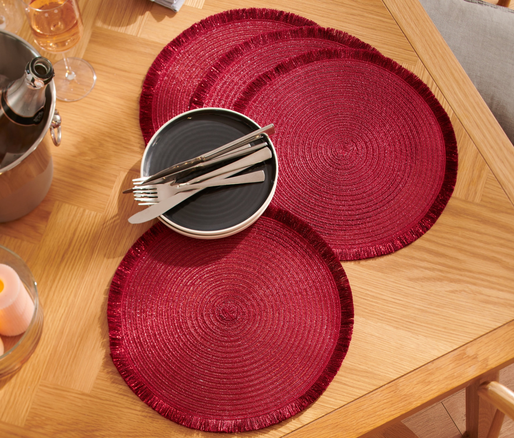 Štyri červené prestierania na drevenom stole s tanierom, príbory, pohármi a chladičom šampanského.