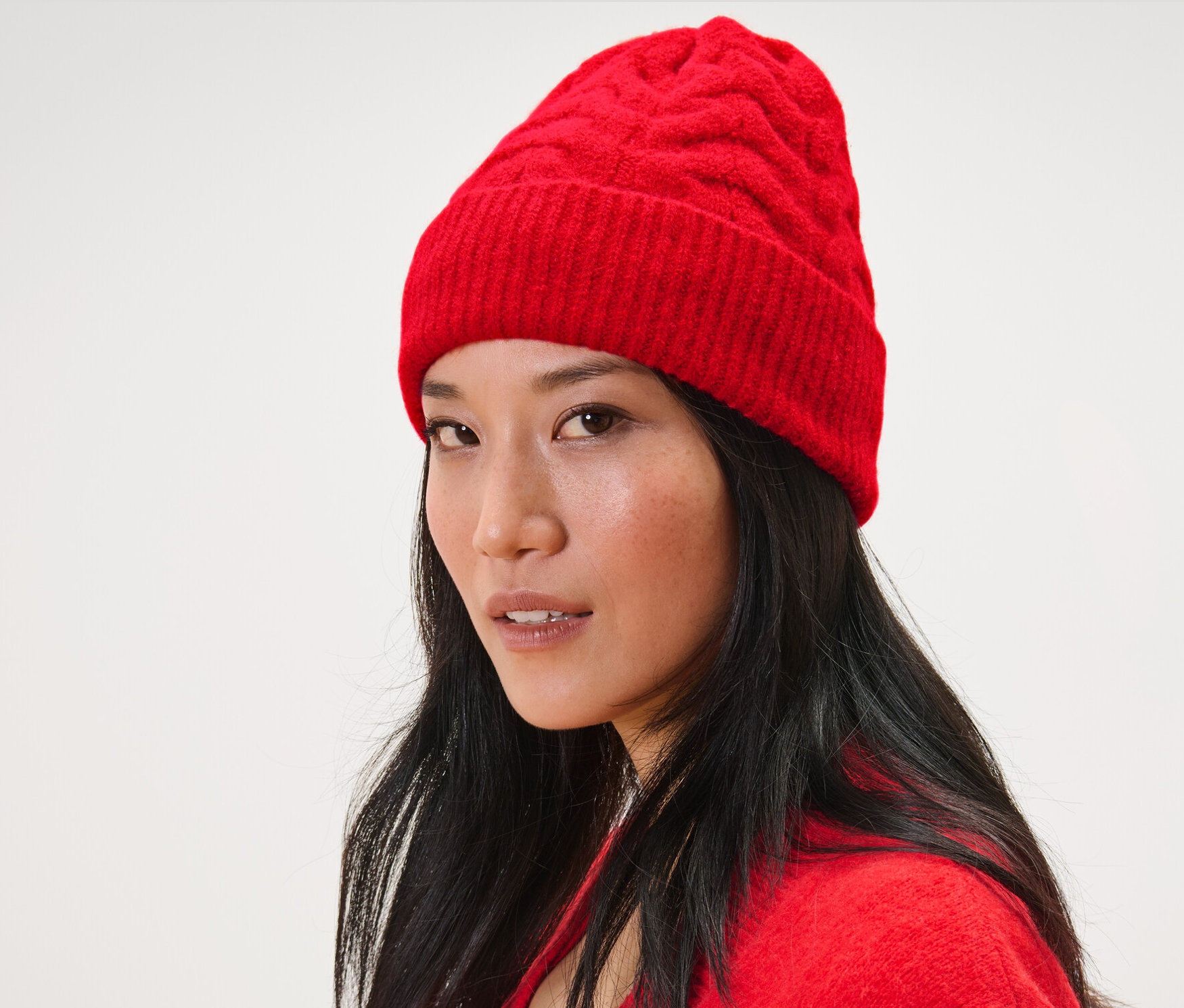 Žena s tmavými vlasmi nosí červenú pletenú čiapku s vrkočovým vzorom a červený kardigán.