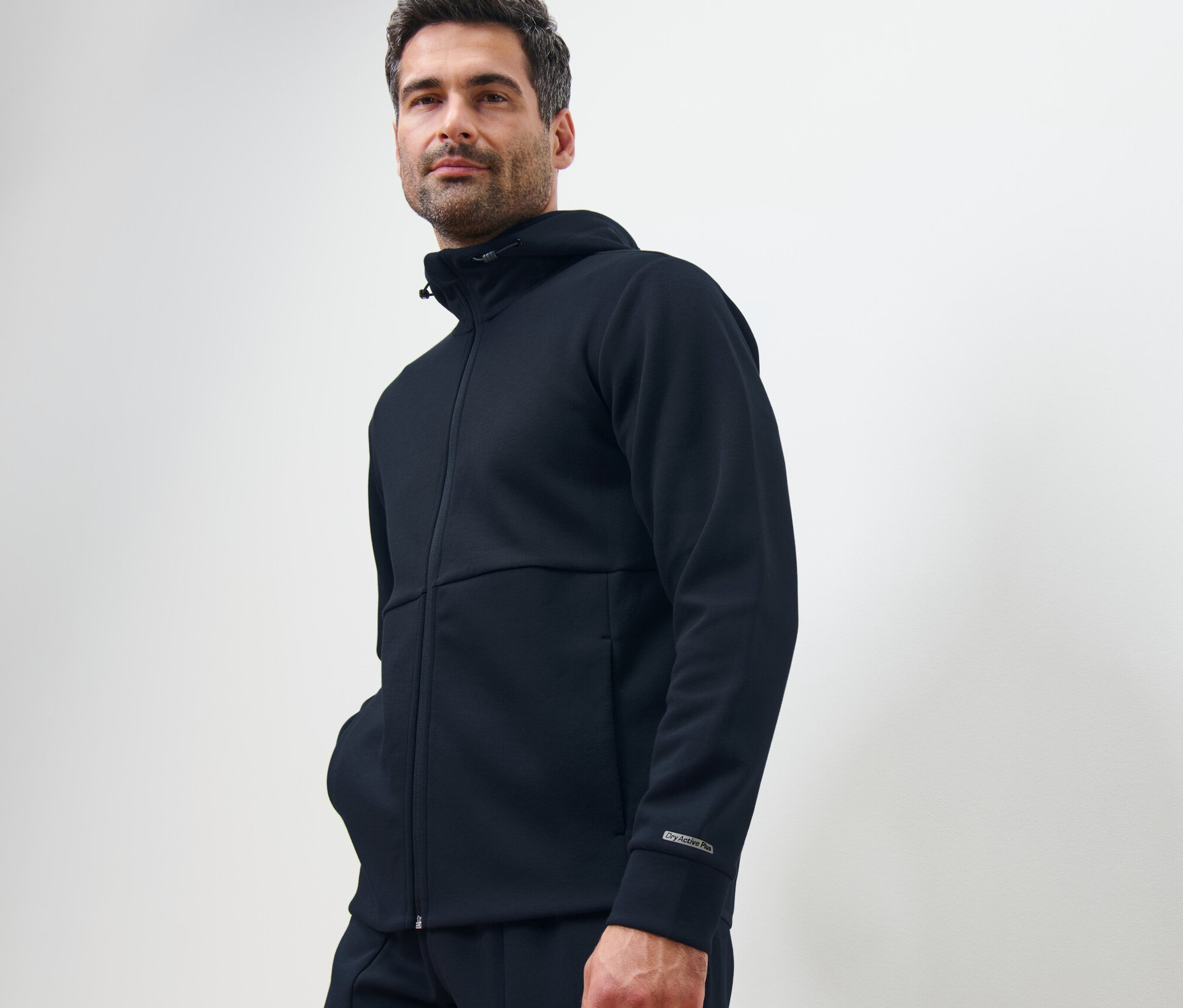 Muž pózuje v tmavomodrej funkčnej teplákovej mikine.