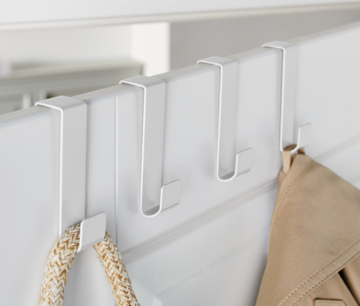 Na bielych dverách sú zavesené tri biele háčiky na dvere, na ktorých visí bunda a taška.