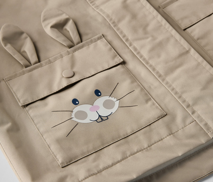 Detail detskej hnedej bundy do dažďa s vreckom s tvárou králika.