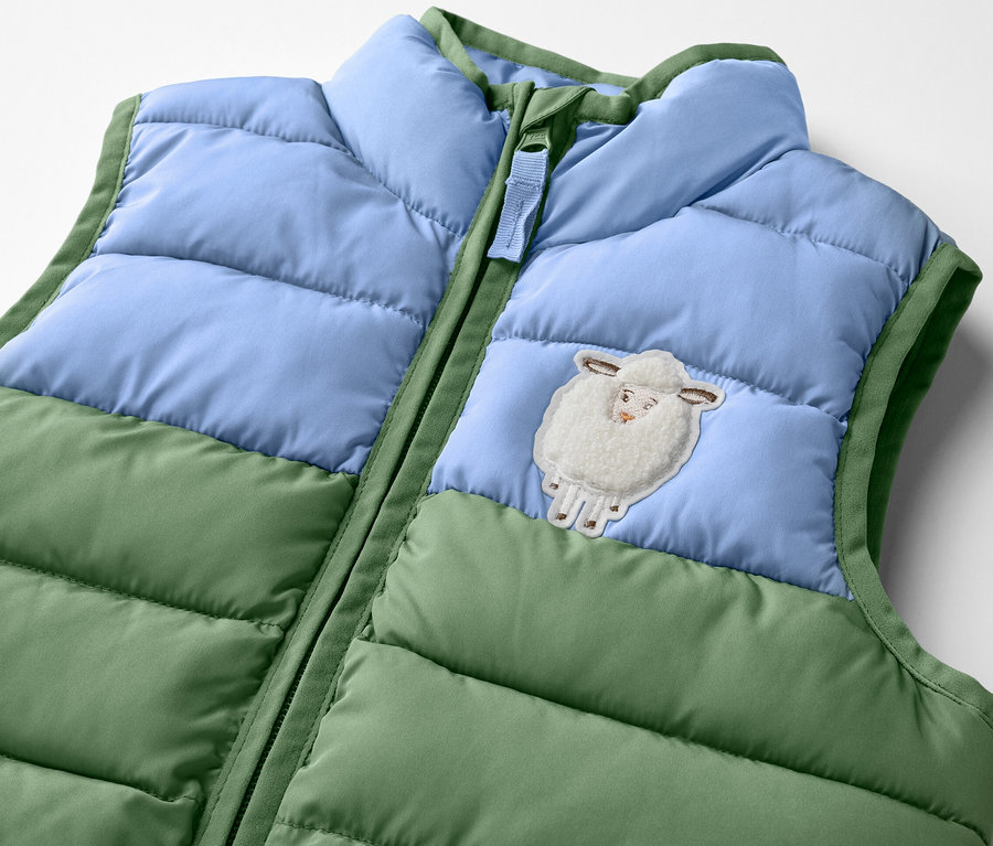 Detail detskej prešívanej vesty, colorblocking, s nášivkou ovečky.
