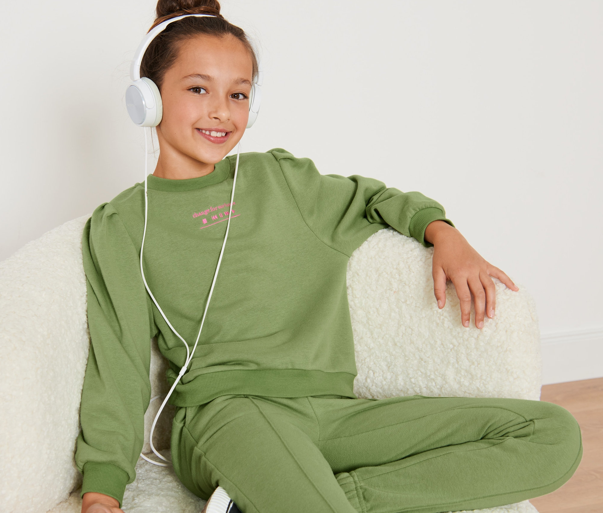 Dievča sedí v kresle a má na sebe detskú skrátenú mikinu a slúchadlá.