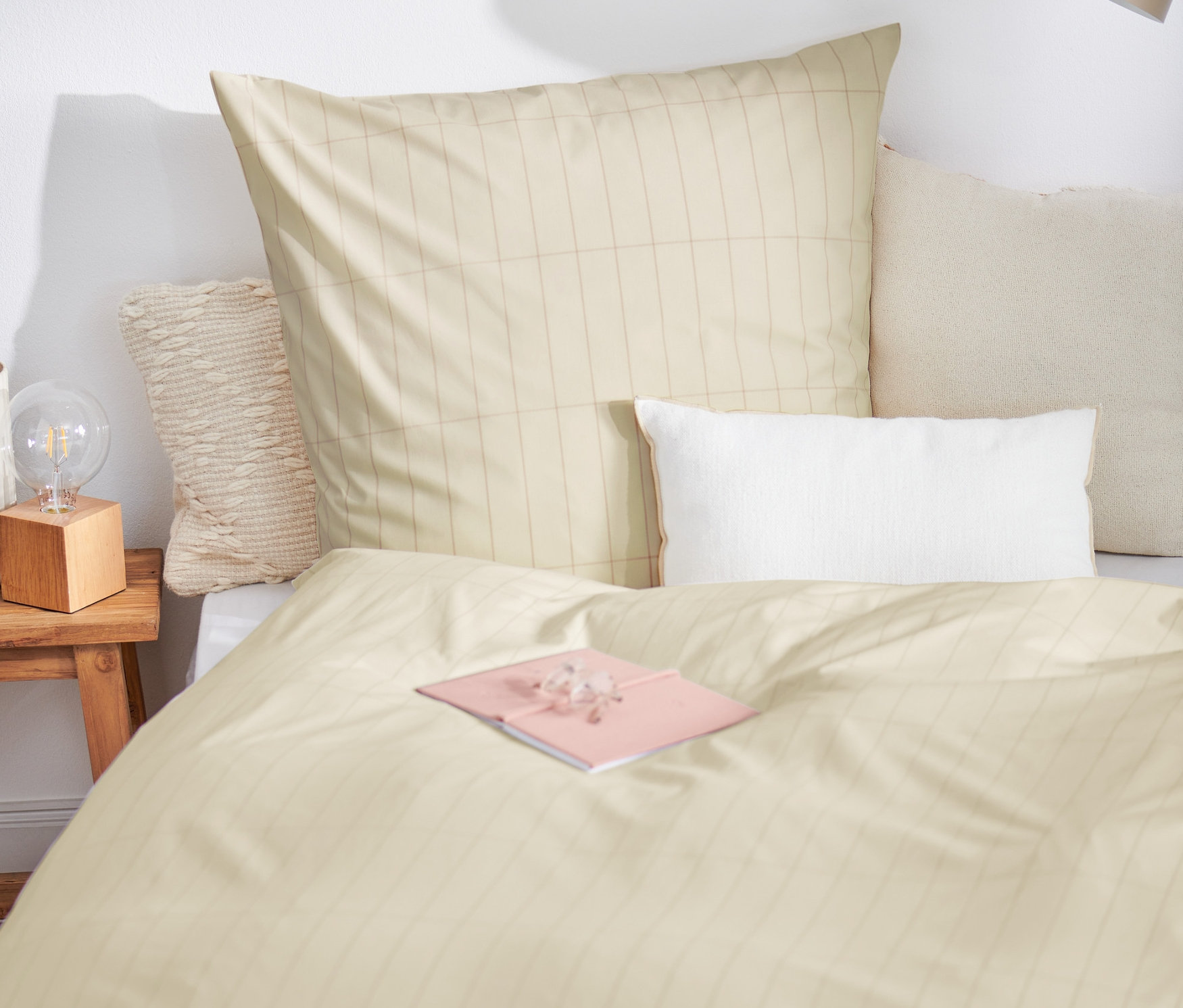 Na posteli leží prémiová bavlnená posteľná bielizeň štandardnej veľkosti a ružový zápisník.