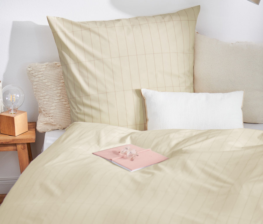 Na posteli leží prémiová bavlnená posteľná bielizeň štandardnej veľkosti a ružový zápisník.