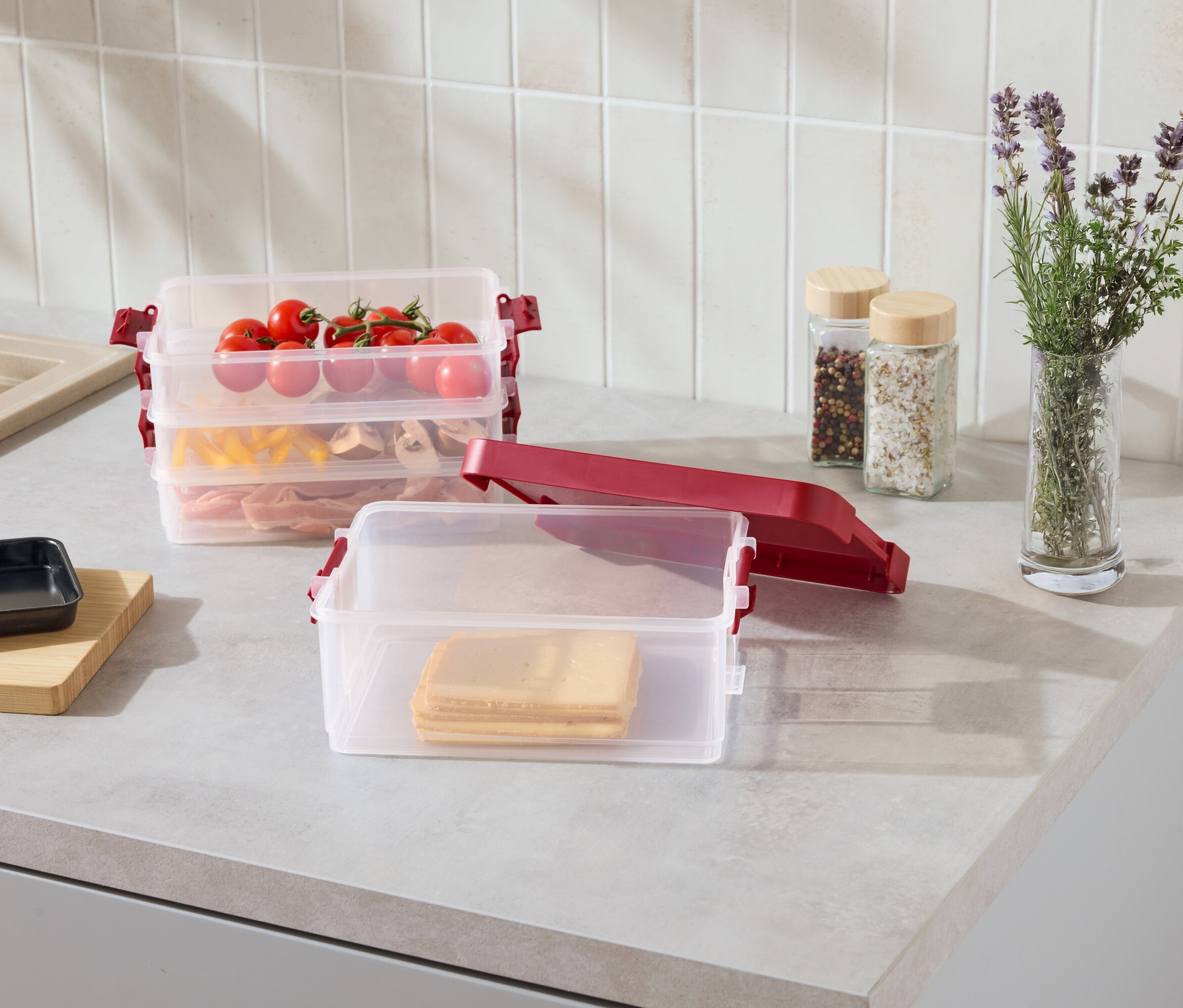 Na kuchynskej linke sú priehľadné stohovateľné nádoby s červenými sponami, naplnené plátkami syra, cestovinami, mäsom a paradajkami.