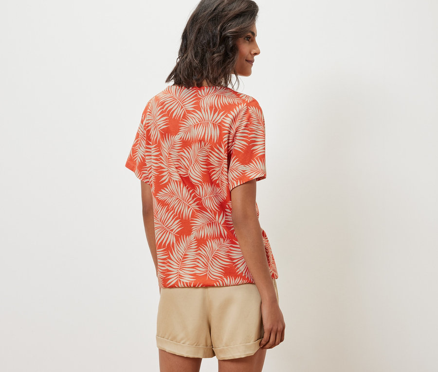 Žena má na sebe vzorované blúzkové tričko a šortky.