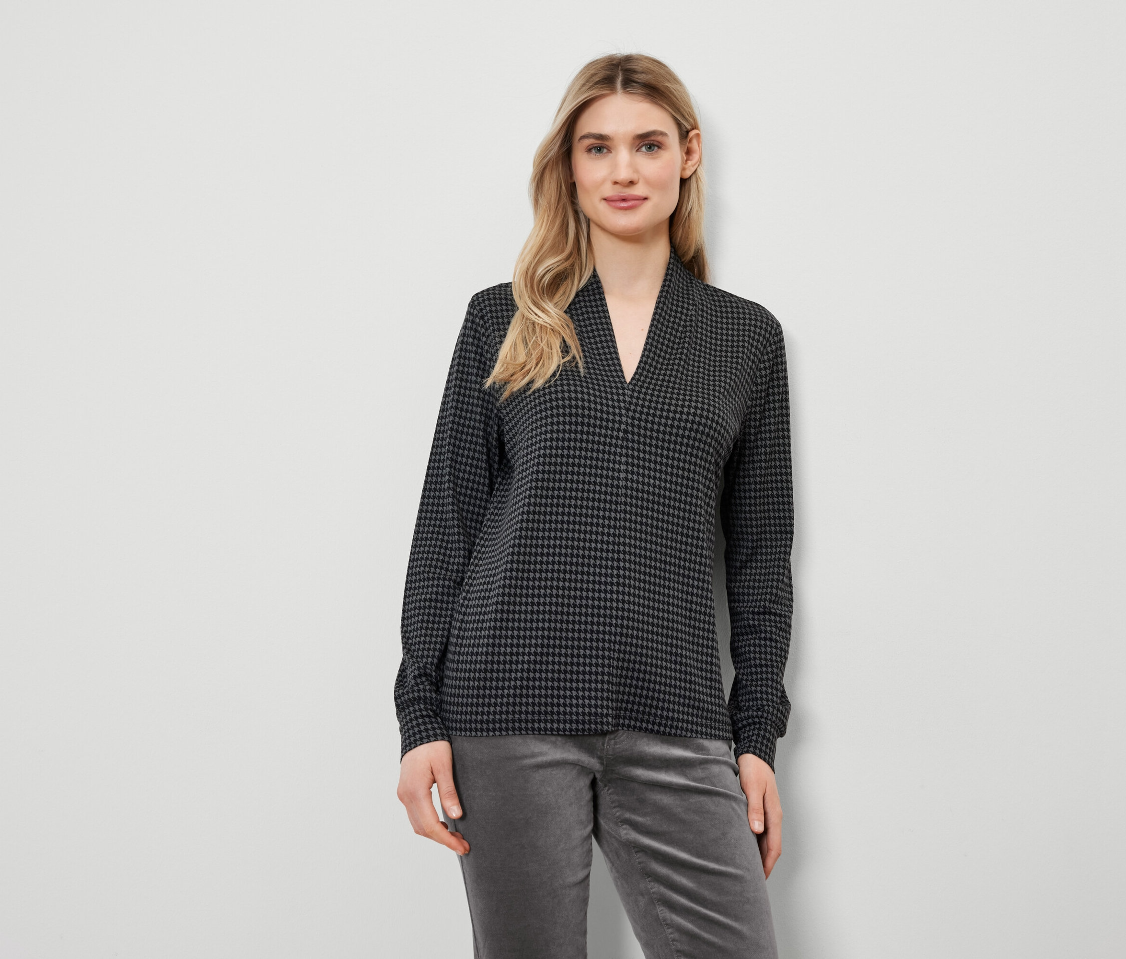 Blondínka má na sebe top s kohútím vzorom a sivé nohavice.