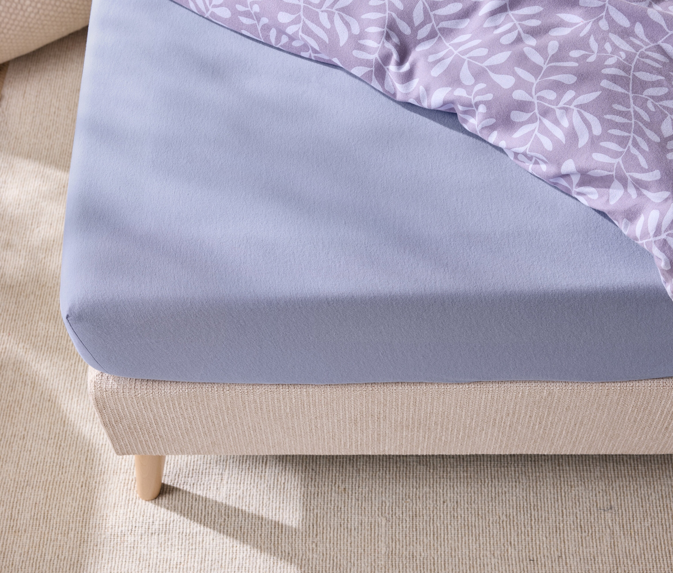 Detail postele s modrou plachtou a posteľnou bielizňou s listovým vzorom.