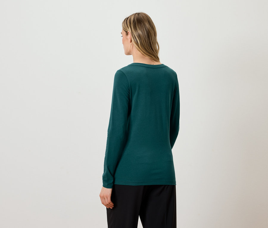 Zozadu je vidieť žena s blond vlasmi, ktorá má na sebe zelené tričko s dlhým rukávom a čierne nohavice.