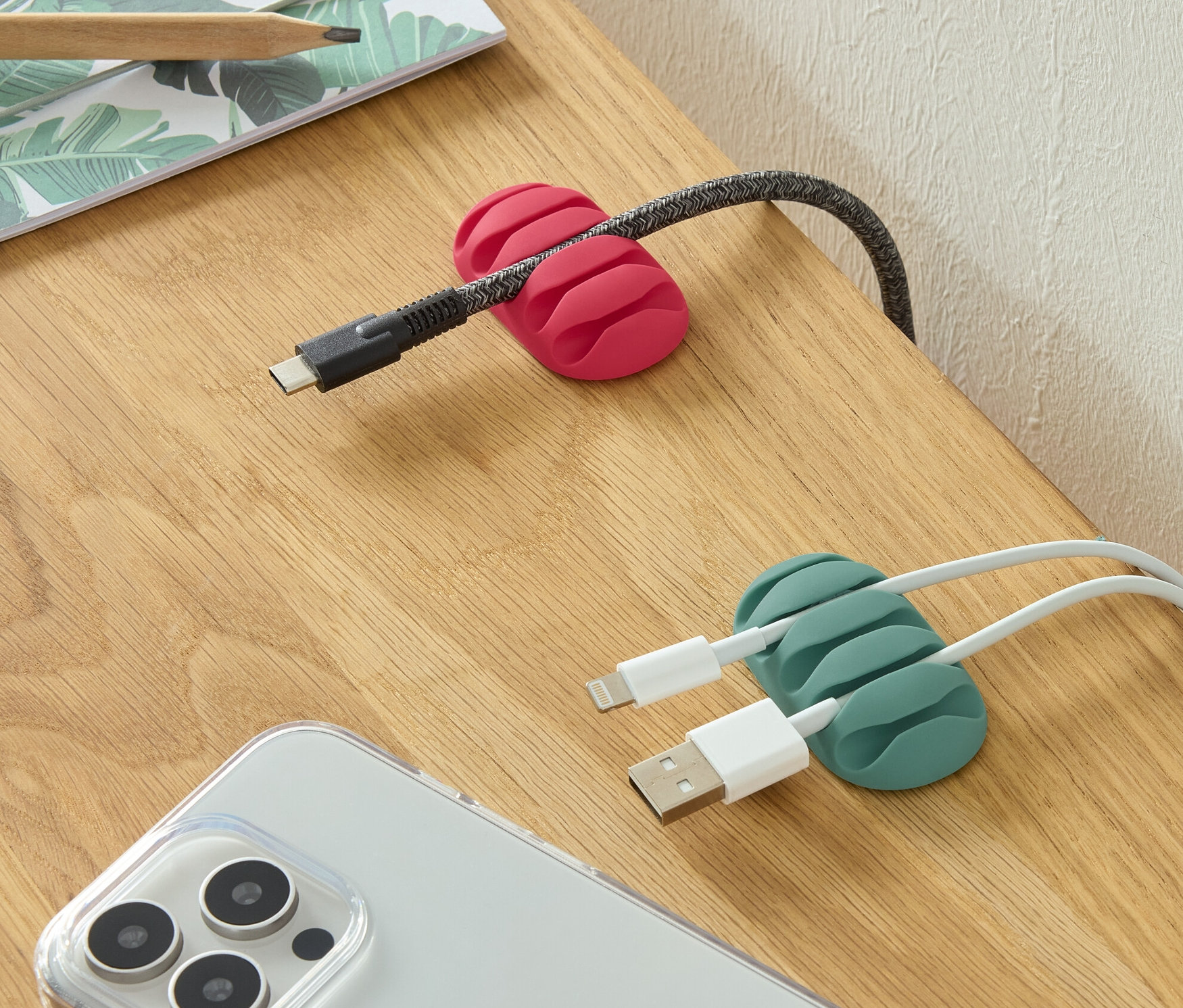 Na stole ležia dva univerzálne organizéry káblov, jeden ružový a jeden zelený, spolu s telefónom a ceruzkami.