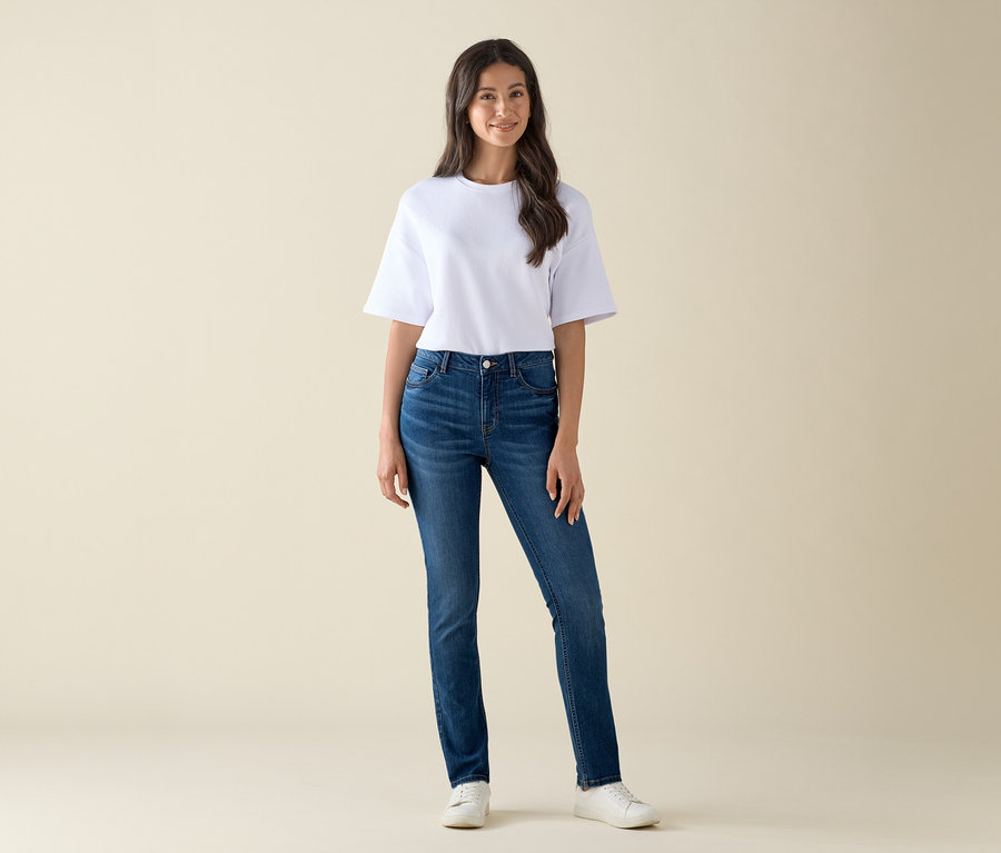 Žena stojí a má na sebe slim džínsy – strih »Emma«, modrý denim a biele tričko.