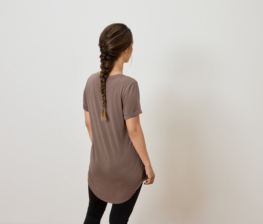 Žena s vrkočom a hnedým tričkom pózuje chrbtom ku kamere.