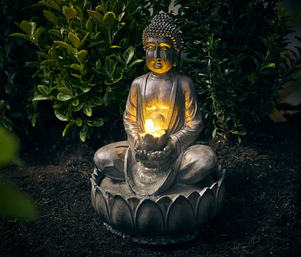 Záhradná fontána Buddha sedí na zemi pred kríkom.