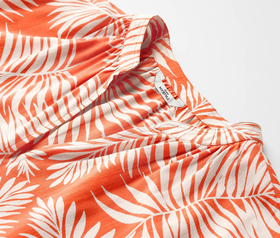 Detail oranžovej blúzky s krátkym rukávom a potlačou listov.