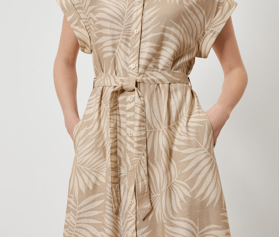 Žena pózuje v ľanových šatách s potlačou listov a rukami vo vreckách.