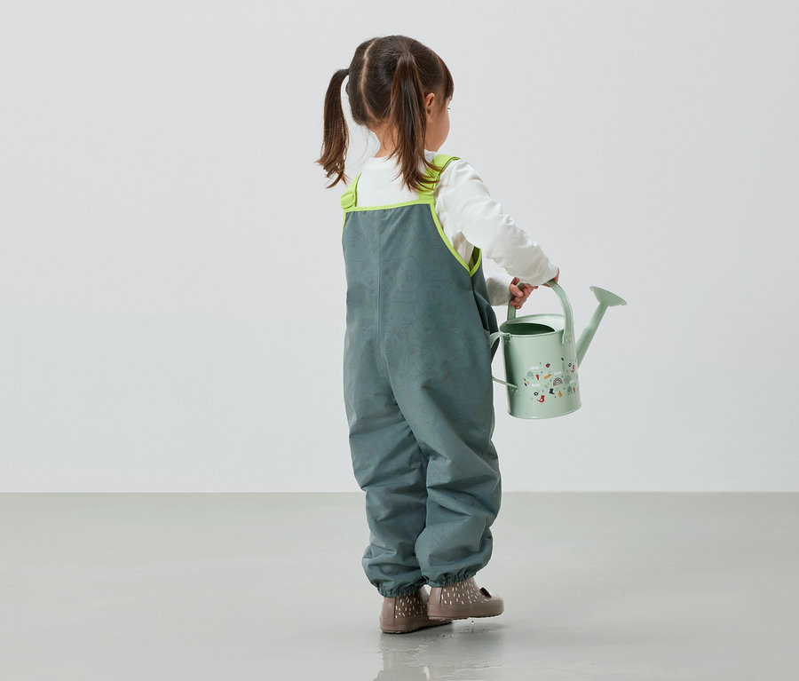 Dievčatko v sivých nohaviciach drží v ruke zelenú kanvicu.