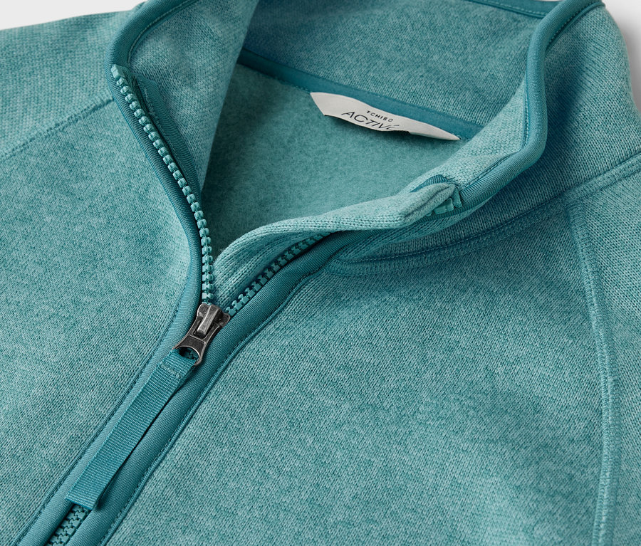 Detailný záber na modrozelenú fleecovú mikinu na zips.