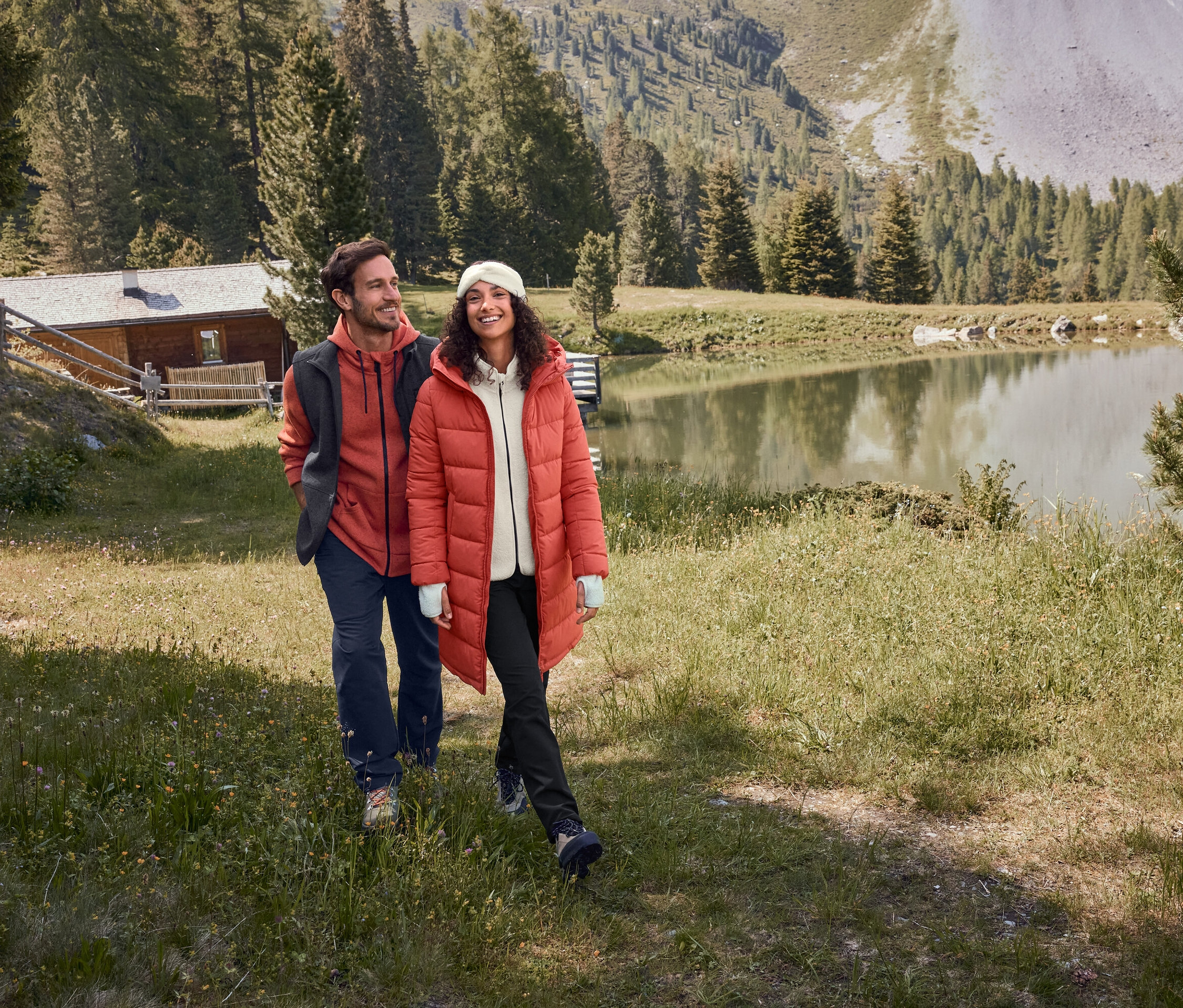 Muž a žena v červených bundách kráčajú po tráve pri jazere.