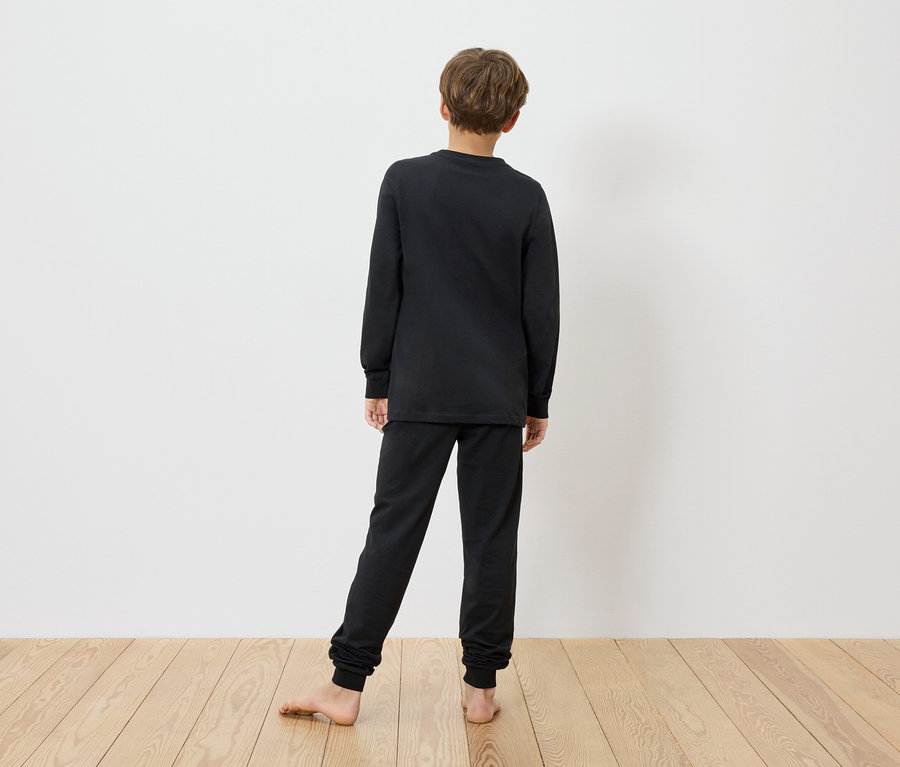 Dieťa stojí bosé pred bielou stenou a má na sebe čierne detské pyžamo MINECRAFT.