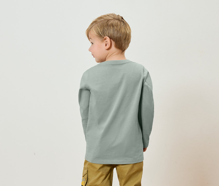 Pohľad zozadu na dieťa s blond vlasmi v sivom tričku s dlhým rukávom a khaki nohaviciach.