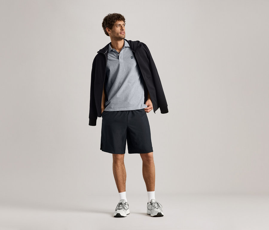 Muž má na sebe mikinu, sivé polo tričko a šortky.