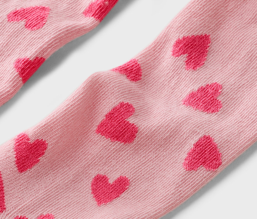 Detailný záber na svetloružové ponožky s červeným vzorom srdiečok.