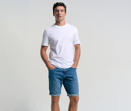 Muž v bielom tričku a džínsových šortkách Tom Tailor TTJOSH REGULAR SLIM, mid stone bright blue denim, s rukami vo vreckách.