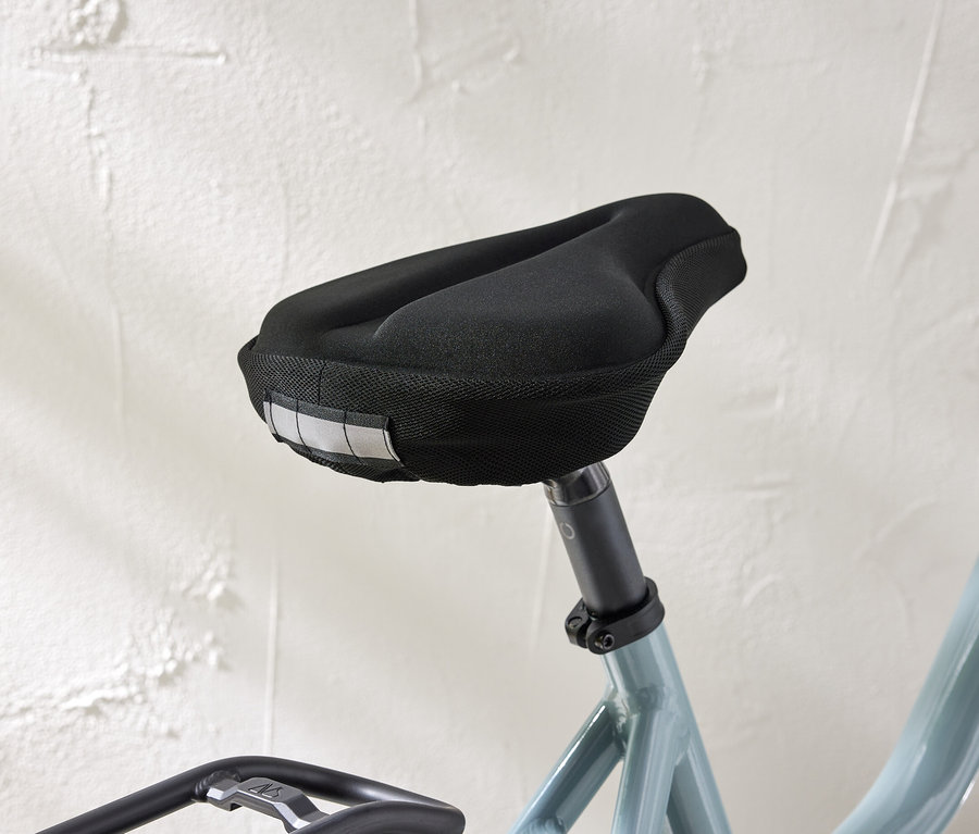 Detail záberu sedadla na bicykel s čiernym poťahom a reflexnými pásikmi na bielom pozadí steny.