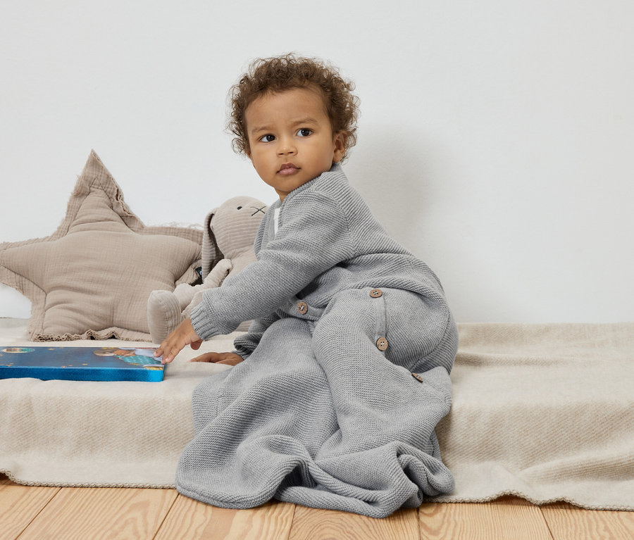 Dieťa sedí na béžovej deke vedľa plyšovej hviezdy a zajačika a dotýka sa modrej knihy.