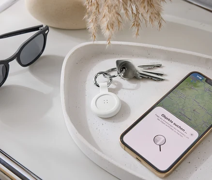 Na podnose ležia slnečné okuliare, kľúče, biely tracker a smartfón s mapovou aplikáciou.