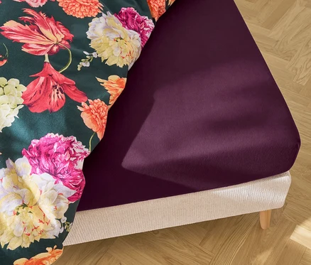 Detailný záber postele s tmavofialovou plachtou a prikrývkou s kvetinovým vzorom.