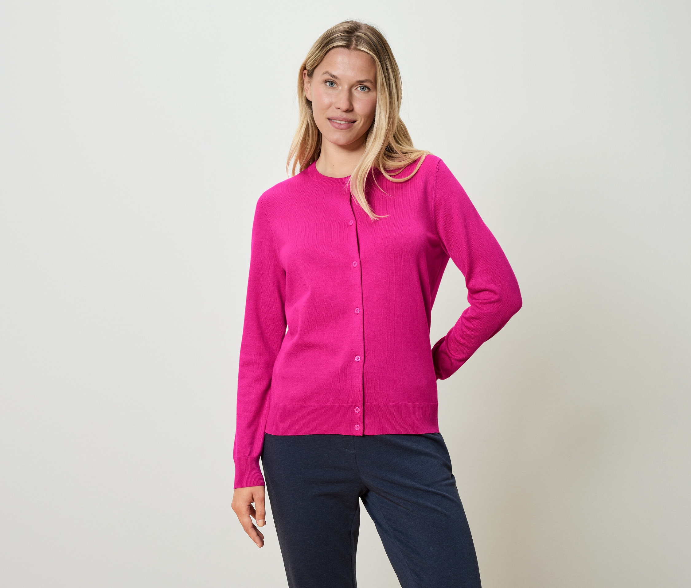 Žena má na sebe ružový kardigán a modré nohavice.