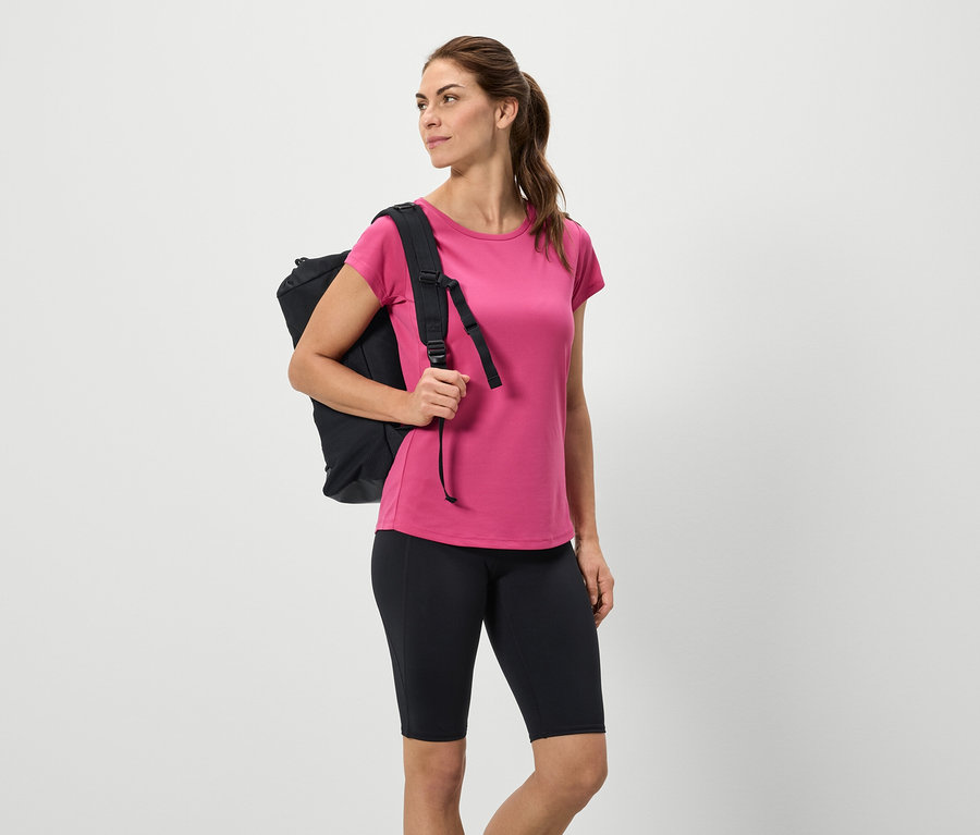 Žena s čiernym ruksakom, ružovým tričkom a čiernymi šortkami.