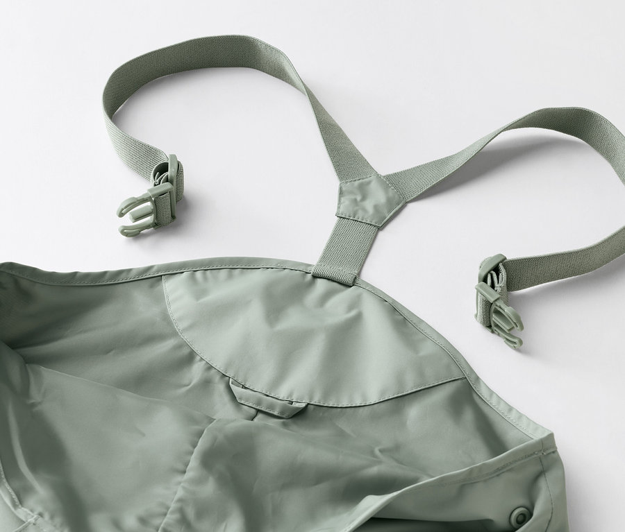 Detailný záber na zelené nepremokavé nohavice s trakmi a prackami na bielom pozadí.