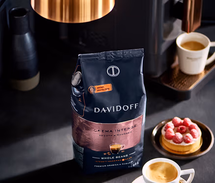 Balíček DAVIDOFF CAFÉ Crema Intense 1000 g zrnkovej kávy stojí vedľa šálky kávy a malinového koláča.