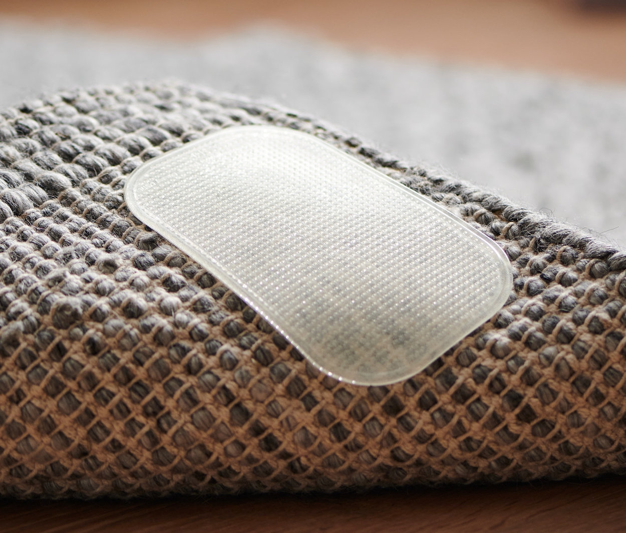 Detailný záber na rohovú časť sivého koberca s jednou priehľadnou protišmykovou podložkou pod koberce, 4 ks.