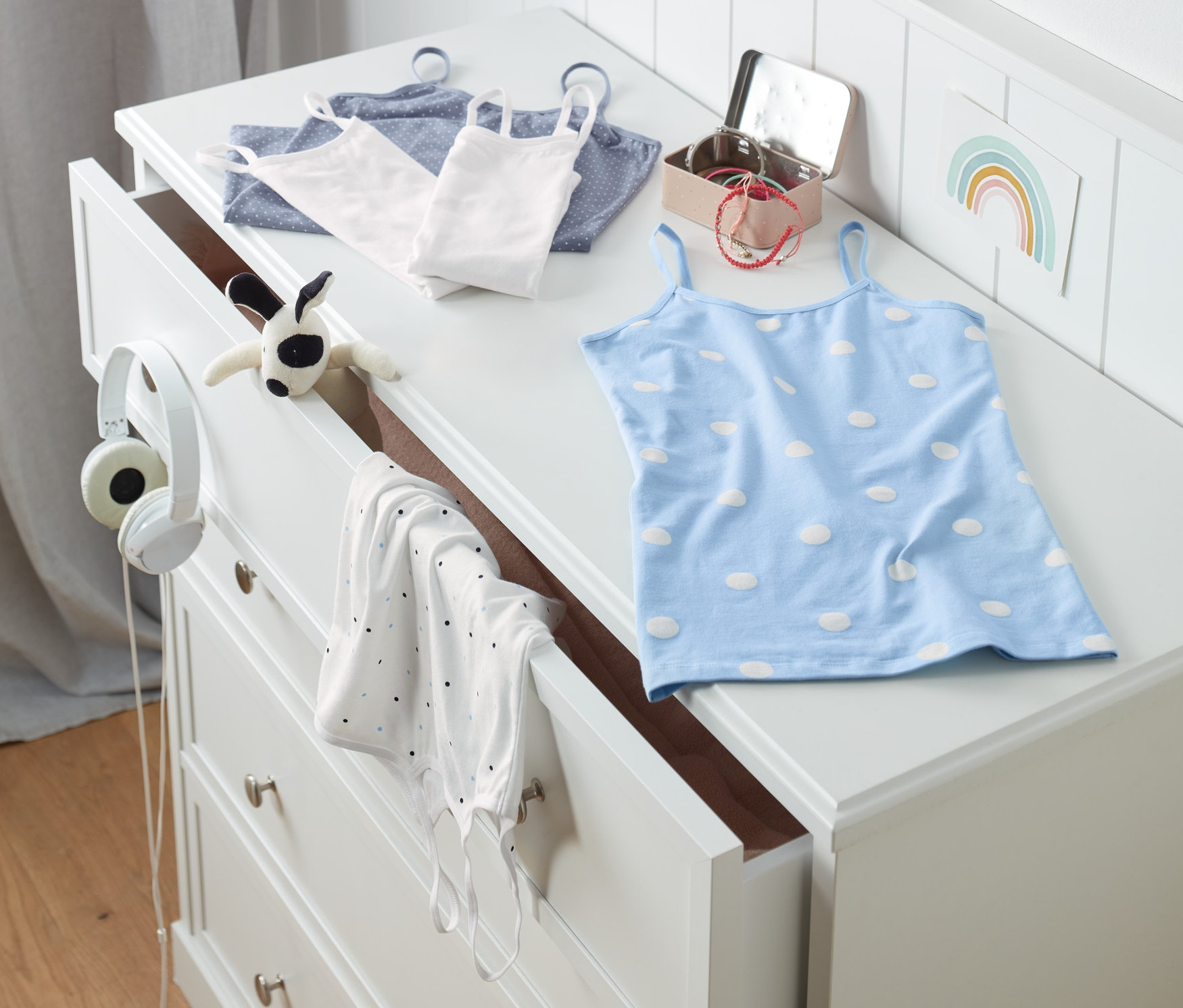 Na komode ležia dievčenské tielka, 5 ks, vrátane jedného modrého s bielymi bodkami.