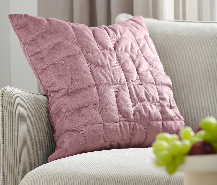 Staroružová zamatová obliečka na dekoračný vankúš leží na béžovej pohovke vedľa misy s ovocím.