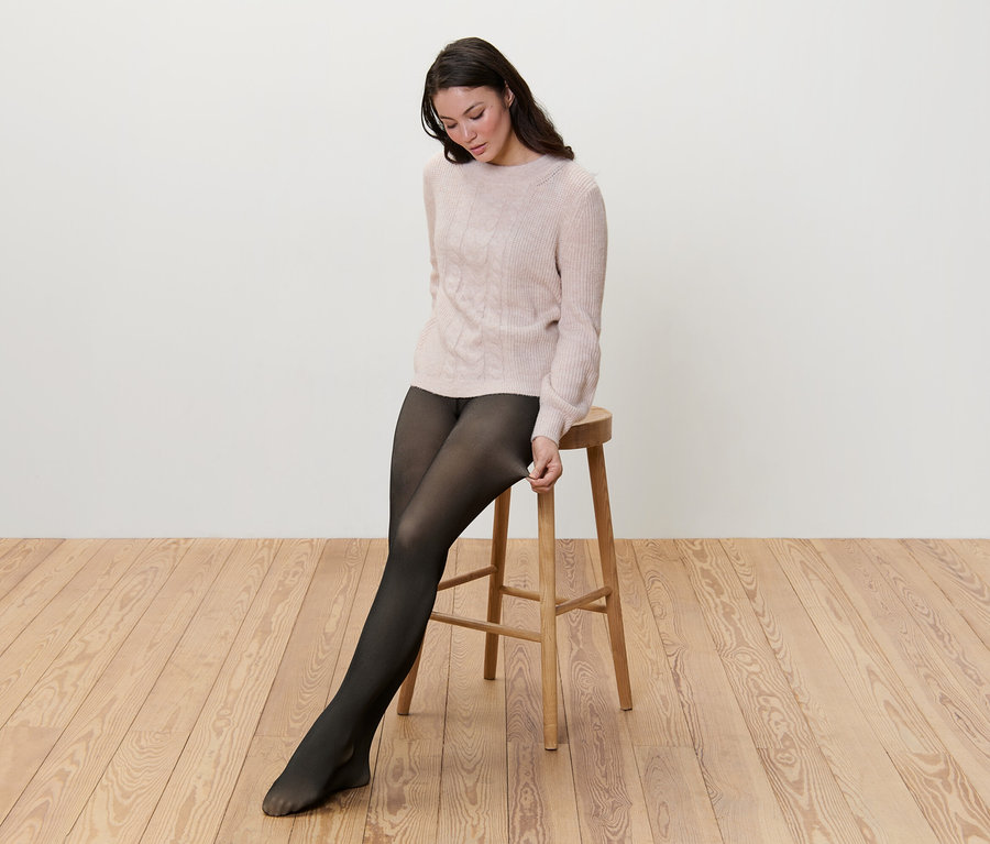 Žena sedí na stoličke a naťahuje si podšité jemné priehľadné pančuchové nohavice.