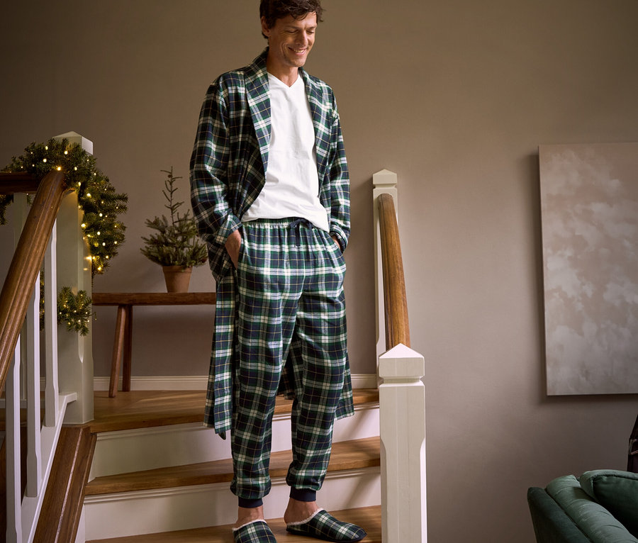 Muž schádza po schodoch v kockovanom flanelovom župane, flanelových nohaviciach, papučkách a tričku s výstrihom do V.