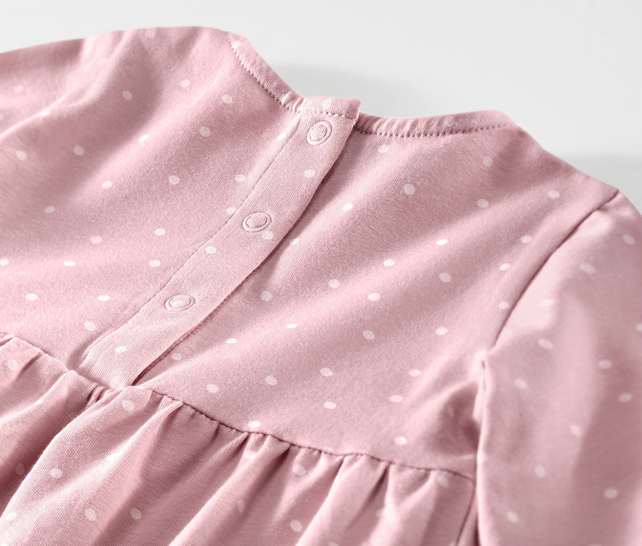 Detail ružových dojčenských džersejových šiat s bielymi bodkami a zapínaním na gombíky.