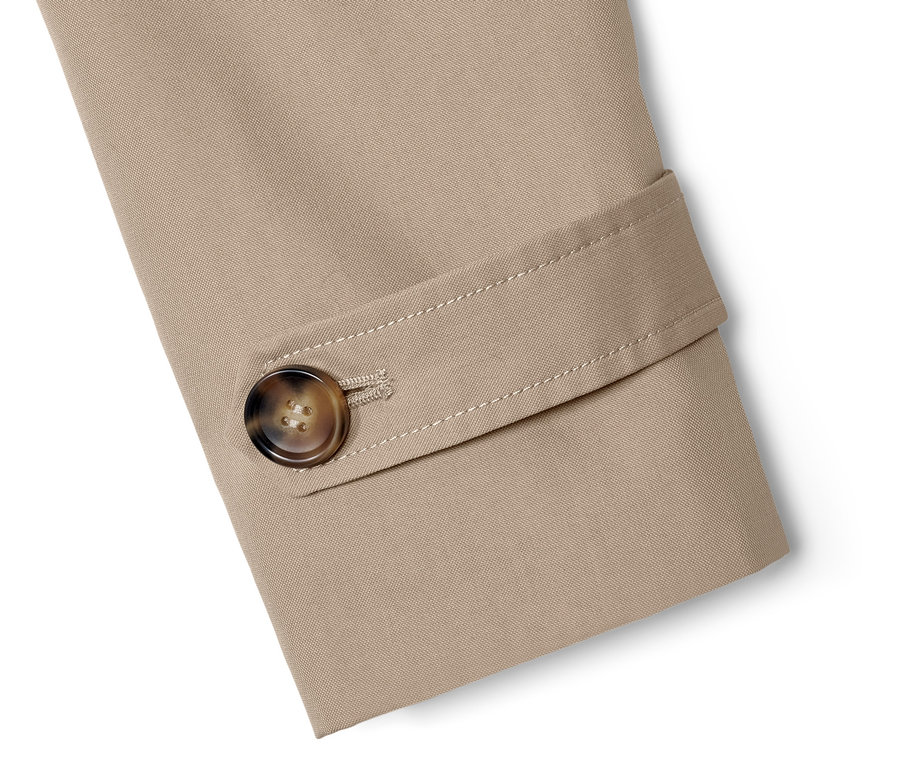 Detail béžového trenčkotu s hnedým gombíkom.