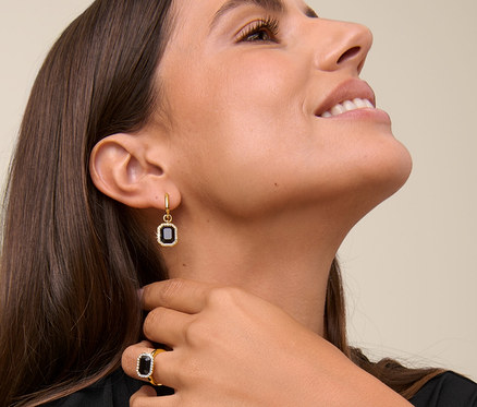 Žena sa usmieva a dotýka sa krku, má na sebe retiazku Royal Black, kruhové náušnice Royal Black a prsteň Royal Black.