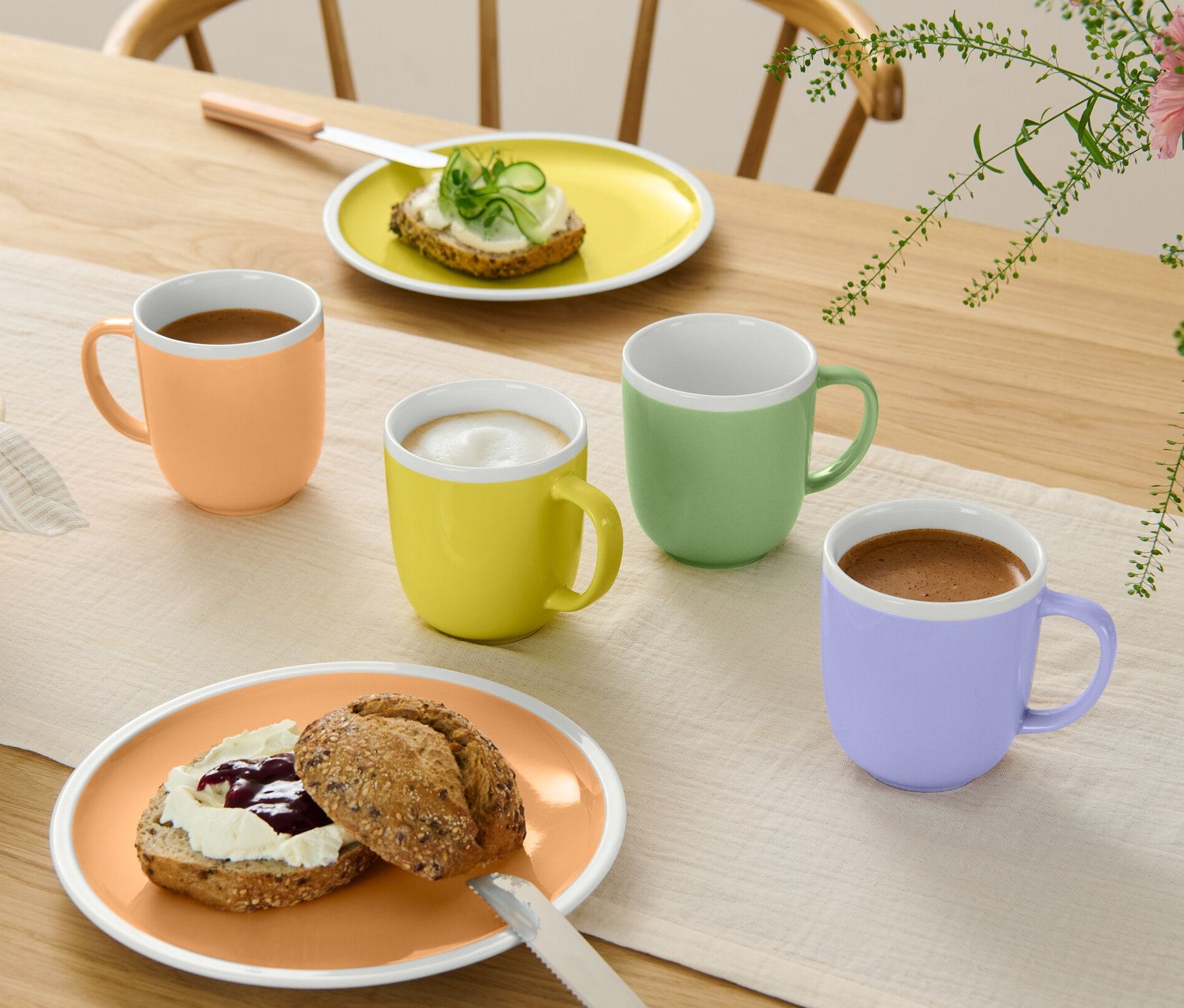Štyri hrnčeky rôznych farieb stoja na stole vedľa tanierov s jedlom.