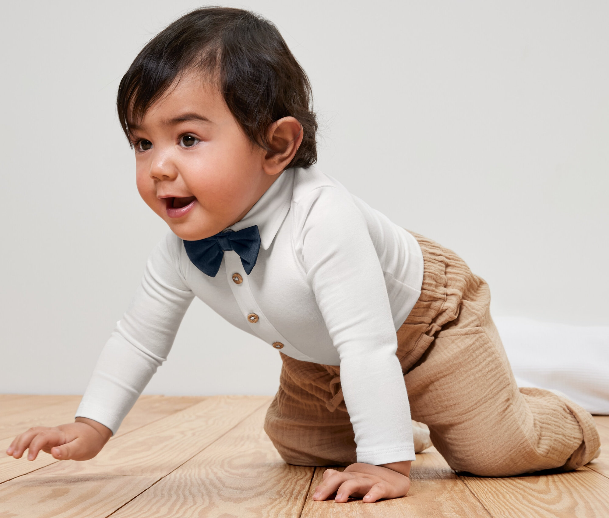 Dieťa lezie v detskom body s motýlikom po drevenej podlahe.